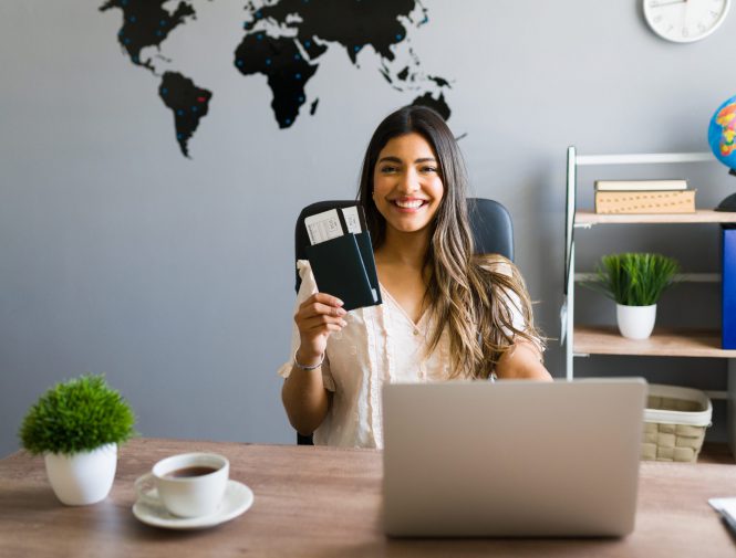 I am here to help you with your booking and travel questions. Female sales agent holding plane tickets while smiling and making eye contact at the travel agency